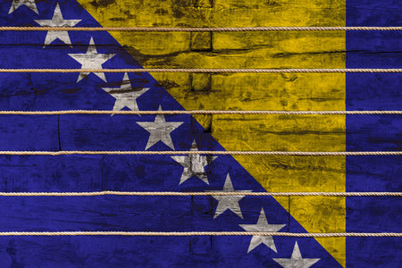 National flag  of Bosnia Herzegovina on a wooden wall background. The concept of national pride and a symbol of the country. Flags painted on a wooden fence with a ropeの写真素材