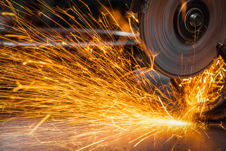 Close-up on the sides fly bright sparks from the angle grinder machine. A young male welder in a...