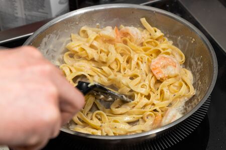 close-up male chef fries large king prawns and pasta in olive oil in a metal pan. The process of making shrimp pastaの写真素材