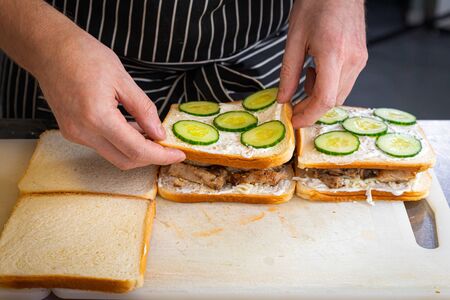 Ð¡lose-up male chef in a black apron puts a burger out of bread, spread with sauce, pieces of meat, cucumbers. The process of preparing fast food, sandwich, burgerの写真素材