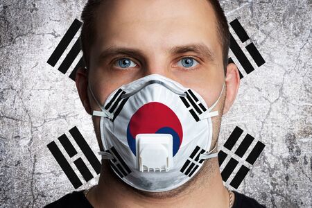 Young man with sore eyes in a medical mask painted in the colors of the national flag of South Korea. Coronovirus disease  COVID-19 concept.  Man is afraid of getting the fluの写真素材
