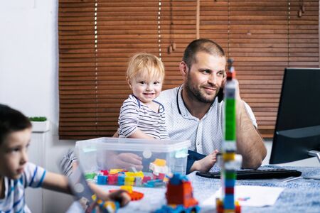 Man working from home during quarantine. Little son sitting on his tables and distracting.Exhausted parent with hyperactive child.の写真素材