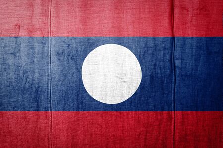 National flag of Laos  depicting in paint colors on old textile. Flag  banner on  fabric texture background.の写真素材