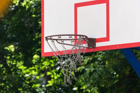 Close-up of a basketball basket with a white net and a white board, in the background green foliage on a warm summer dayの写真素材