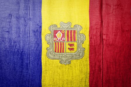 National flag of Andorra depicting in paint colors on old textile. Flag  banner on  fabric texture background.の写真素材