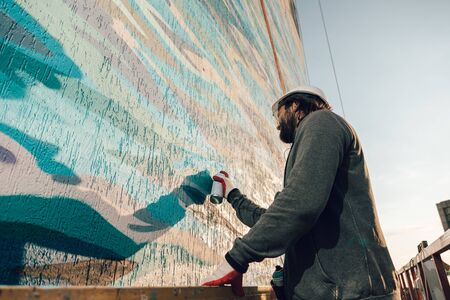 Contractor, artist at high altitude in a building cradle performs facade painting, decorating and home renovation against the backdrop of the city landscape の写真素材