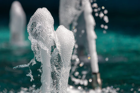 Jets of water with a lot of drops and bubbles under the rays of the sun on a blue background. A...