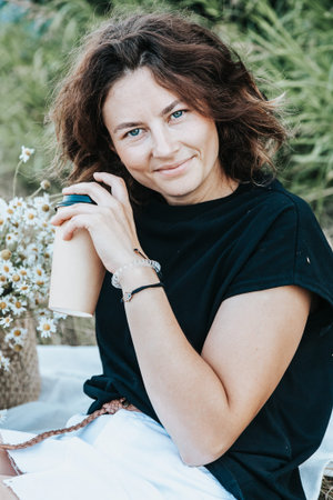 Pretty fresh darkhaired young woman posing against the backdrop of a green tree, holding a wicker...