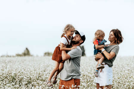 Happy family is playing, having fun on the field with flowers at sunset. Family and love concept. Young family housing conceptの写真素材