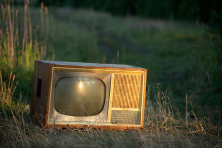 old retro TV set on a field road against a wheat background under the rays of the setting sunの写真素材