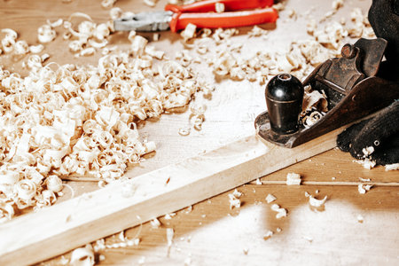 Close up of the a young brunette man builder handles a wooden bar with a black jack plane in the...