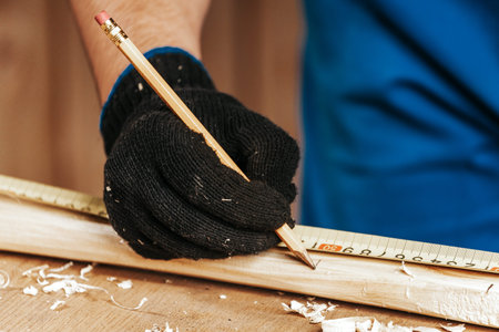 Close-up of a man builder doing the markup on a wooden board with a pencil in a workshop