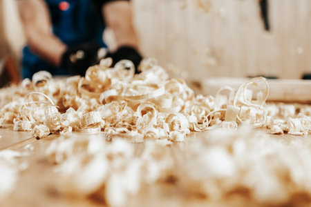 Close-up of a pile of fresh wooden sawdust, in the background a male carpenter works in a workshop,...