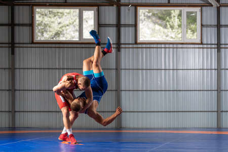 Two strong wrestlers in blue and red wrestling tights are wrestlng on a wrestling carpet in the gym. Young man doing grapple.の写真素材