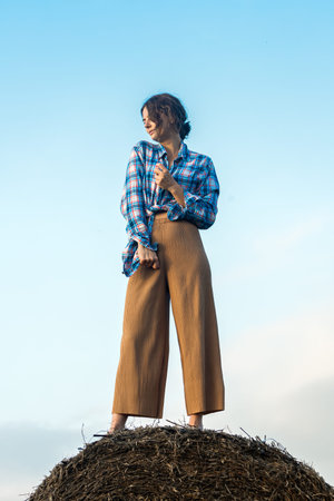 A romantic walk of a curly-haired woman in clothes like a boy standing on a haystack against the...