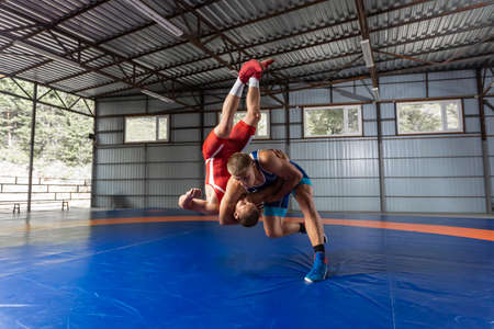 Two strong wrestlers in blue and red wrestling tights are wrestlng on a wrestling carpet in the gym. Young man doing grapple.の写真素材