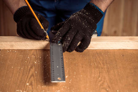 CLose up of the carpenter with a pencil and tape measure mark on wooden board on table. Construction industry, housework do it yoursel. Work with woodenの写真素材