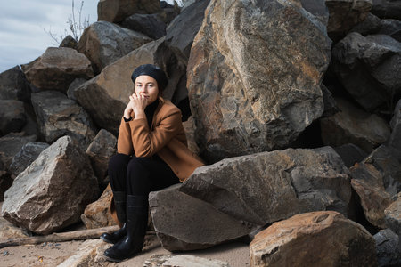 A romantic walk of a curly-haired woman in a black shiny beret and a beige wool coat posing on stone...
