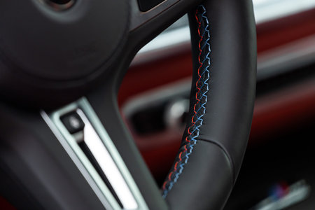 Close-up of a black steering wheel made of soft expensive leather with hand-stitched multicolored...