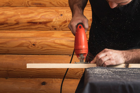 A carpenter using a jigsaw to cut wood cuts bars. Home repair concepts, close up.