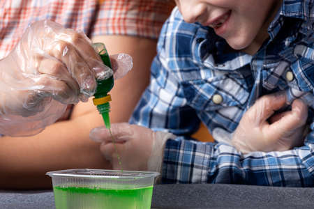 Chemistry education and study concept. close-up mom and her son are dripping a green chemical element into a container for experiments at home. Chemical experiment with polymer wormsの写真素材