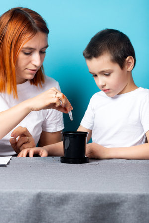 Mom and son use a test tube to make holes in the ground to plant a seed and grow a house plant on the table against a blue background. The concept of gardening classes with children.の写真素材