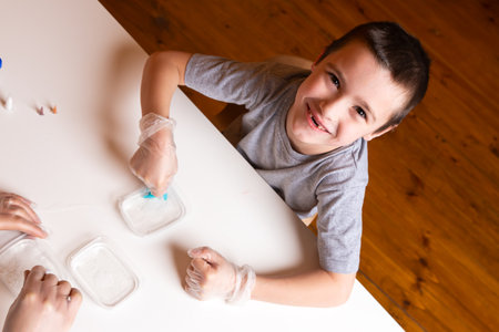 Chemistry education and study concept. Close-up of a smilling boy stirring a mixture with a measuring spoon in a container with chemical elements, for conducting experiments at home, top viewの写真素材