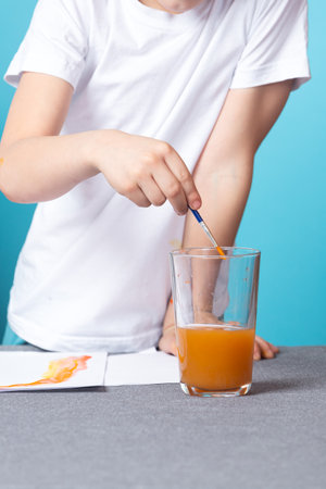 Close-up of a boy in a white t-shirt washes a brush from watercolor paint on a blue backgroundの写真素材