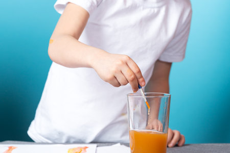 Close-up of a boy in a white t-shirt washes a brush from watercolor paint on a blue backgroundの写真素材