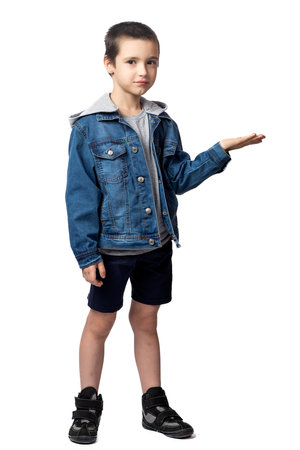 Portrait of smiling boy in denim jacket demonstrates with hand and rejoices, having fun on white isolated backgroundの写真素材