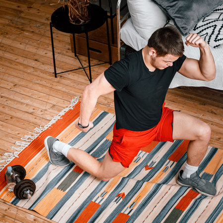 A young man goes in for sports at home, online workout from the laptop. The athlete lunges in the...