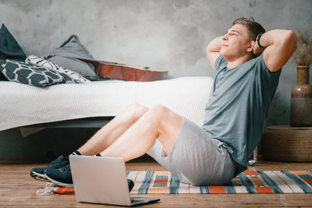 Young man goes in for sports at home, training online. The athlete makes the press, smiles, there is...