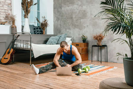 Close-up of a young man in a sports uniform is resting, stretching on the floor at home, watches a movie and studies from a laptop, a social network. Student loafing aroundの写真素材