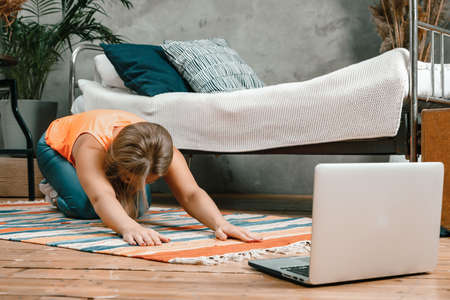 A young woman goes in for sports at home, online workout. The athlete stretching, meditating, sitting on a floor in the bedroomの写真素材