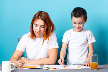 Children's creativity. mom and child son paint watercolor homework for kindergarten on blue backgroundの写真素材