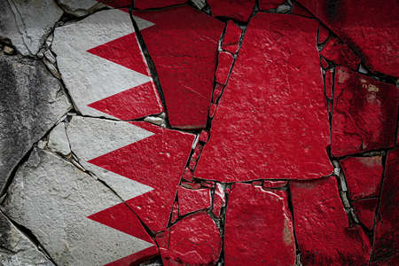 National flag of Bahrain depicting in paint colors on an old stone wall. Flag banner on broken wall background.の写真素材