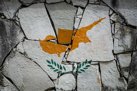 National flag of Cyprus depicting in paint colors on an old stone wall. Flag banner on broken wall background.の写真素材