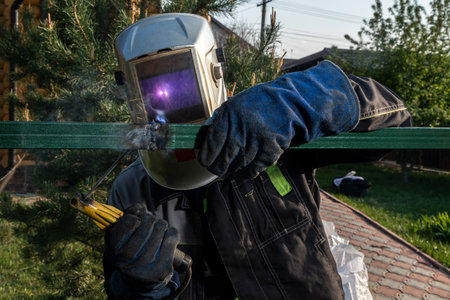 Close up of the a welder welds a fence on the construction site in the village. Construction on a metal frame.の写真素材