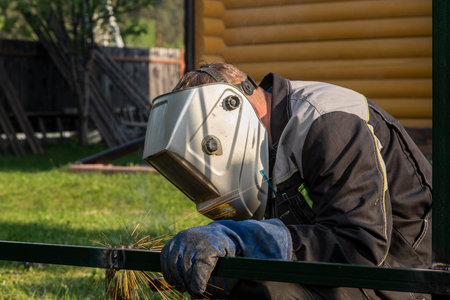 Close up of a young man welder in uniform, welding mask and welders leathers, weld metal with a...