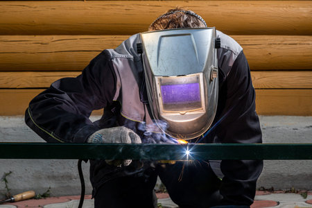 Worker male welder at a construction site welds a metal structure on a fence, welding process...