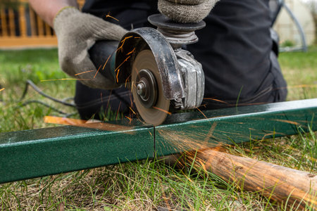 A close-up of a welder using a metal grinder to cut a metal on the grass in the village, bright...