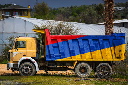 Dump truck with the image of the national flag of Armenia is parked against the background of the countryside. The concept of export-import, transportation, national delivery of goodsの写真素材