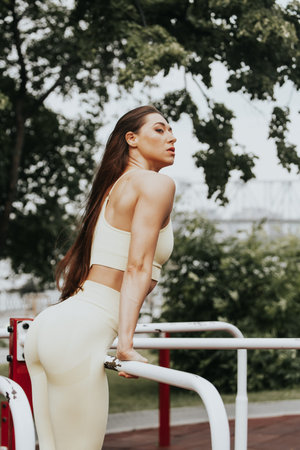 Young woman with long straight hair on street workout pulls up on the uneven bars on the sports...