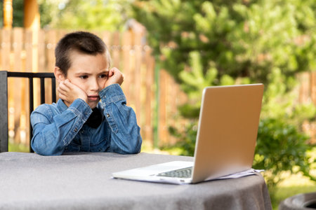 child boy listing to a lecture, is using a laptop and communicates on the Internet at home....