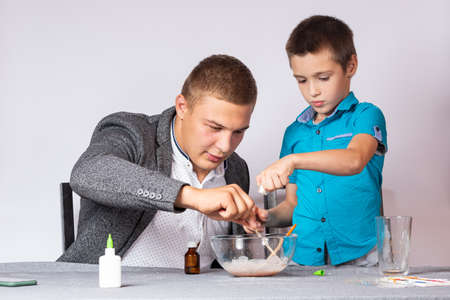 Chemistry education and training concept. Close-up of a boy and his dad doing a home chemical experiment, making slime from glue, sodium tetraborate and dyesの写真素材