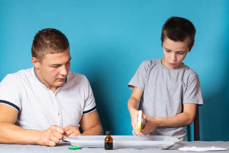 Dad and son are conducting chemical experiments, observing the change in color of a chameleon as a result of the chemical reaction of iodine and starch at home. Boy sprays iodine on a drawingの写真素材