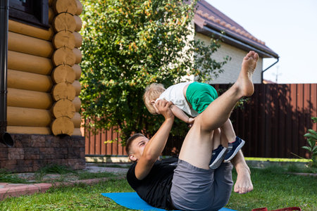 Young dad athlete with his little cheerful son goes in for sports on the mat on a warm day in the...