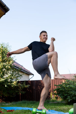 A cheerful athlete with blonde hair lunges, stretching in the garden, next to a laptop with online...