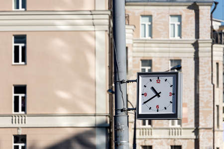 Close-up of a square street clock hanging on a pillar against the background of a brick wall of a buildingの写真素材