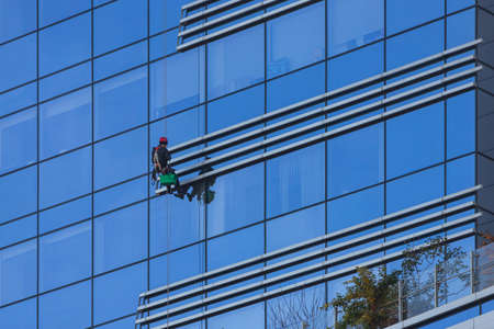 A man cleaning windows on a high rise building. Industrial climber hanging on the clothesline and washes windows, glass facade modern building.の写真素材